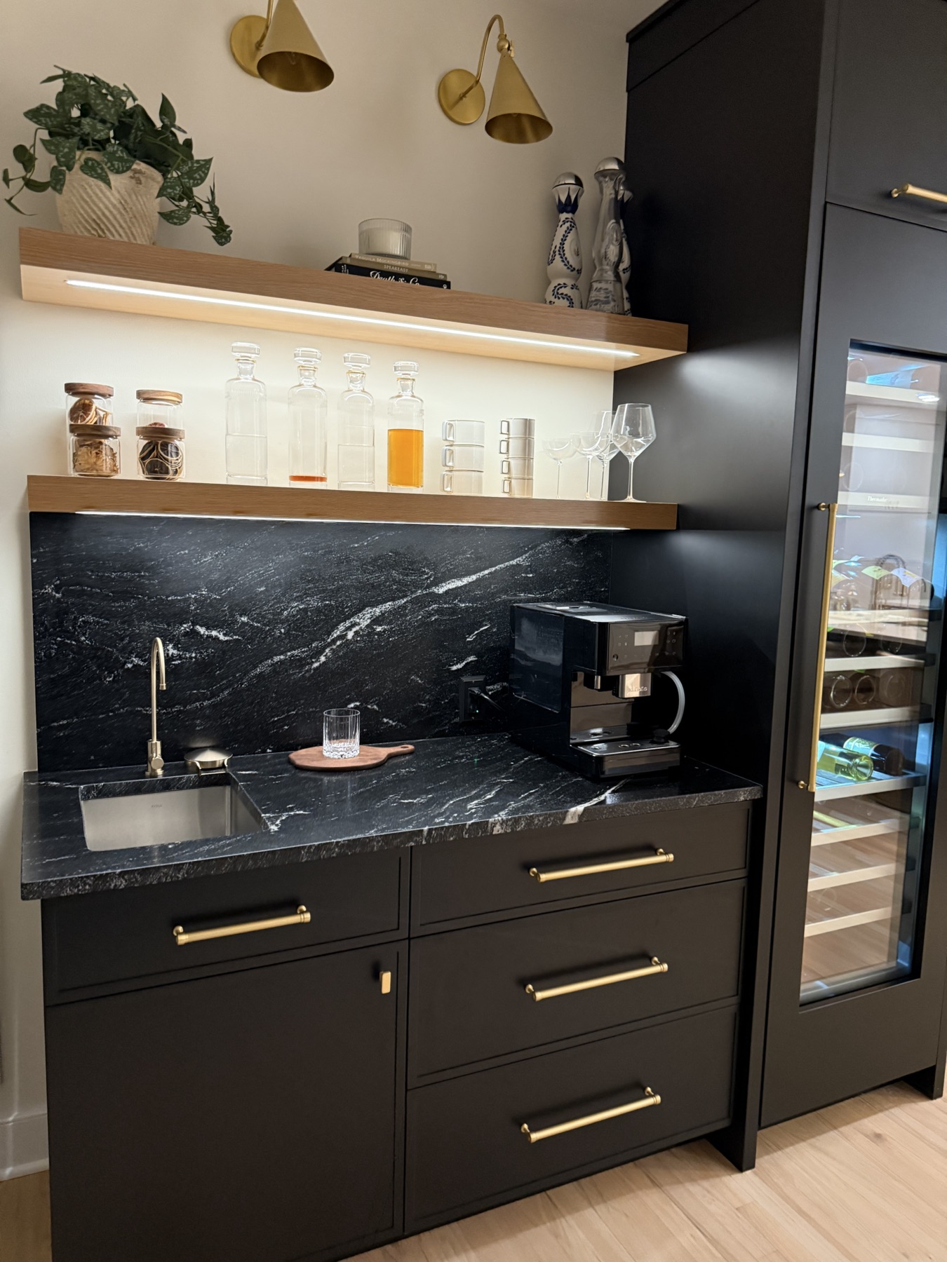 Built-in bar with black cabinetry, stone backsplash, and brass fixtures