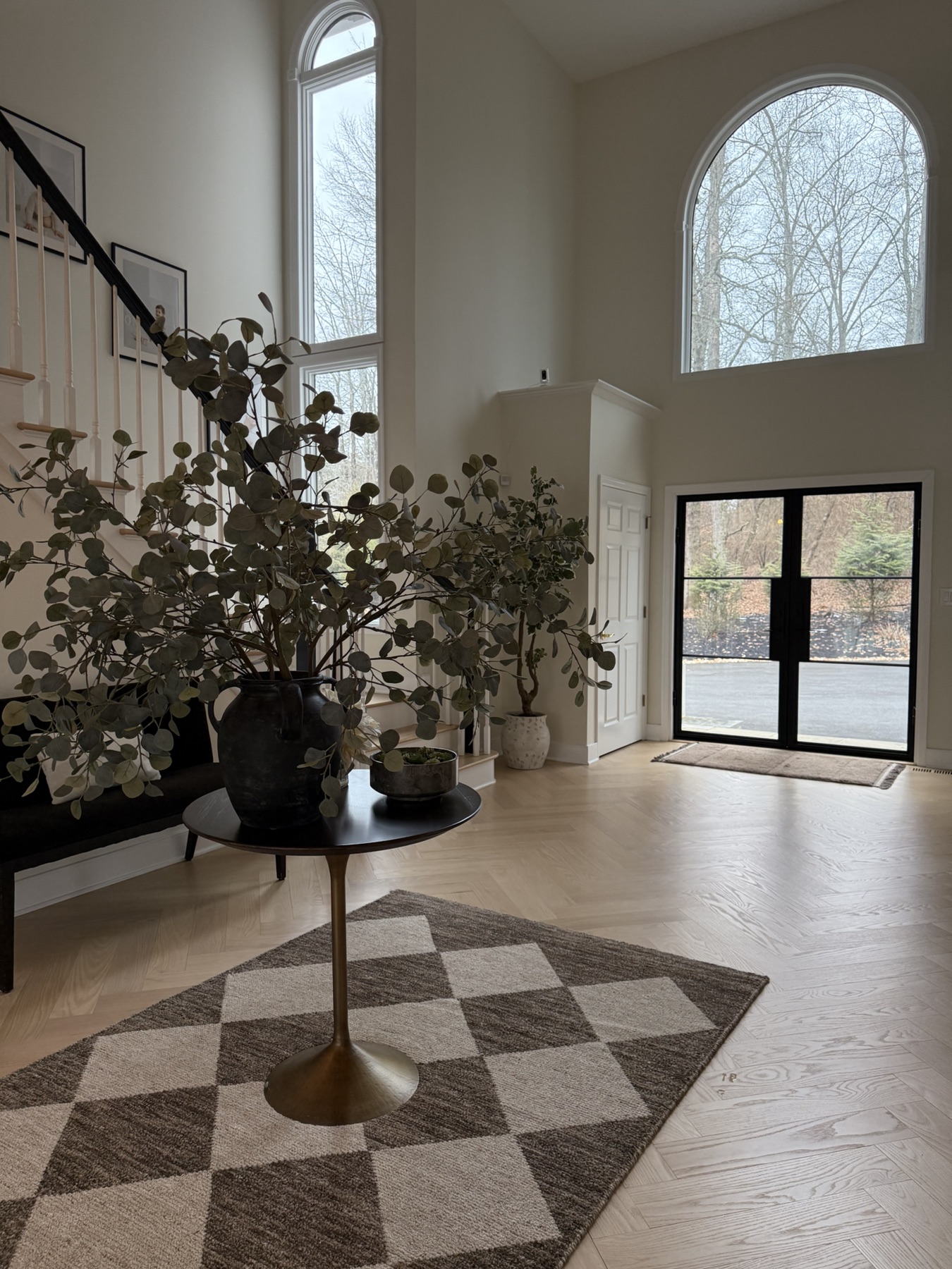 Residential entry with arched windows, black doors, pale wood floors, and styled furnishings